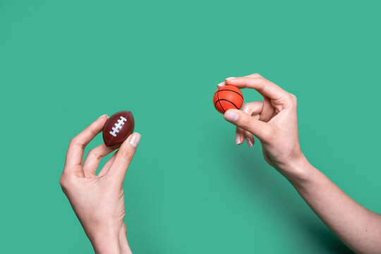 Hands holding miniature american football and basketball on green