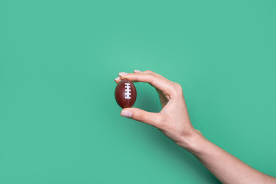 Hand hold miniature American football against green background