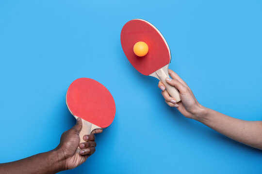 Two players hold ping pong paddles with orange ball