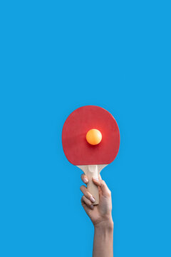 Hand holding red table tennis paddle and orange ball