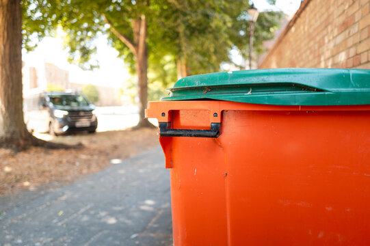 Close-up of a typical commercial waste disposal bin seen in a city centre in the UK. A nearby commercial van is parked in a green space area in the city centre.
