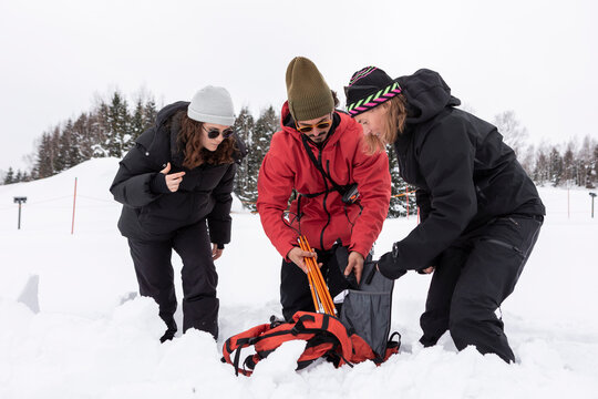 Three adults packing avalanche equipment into backpack