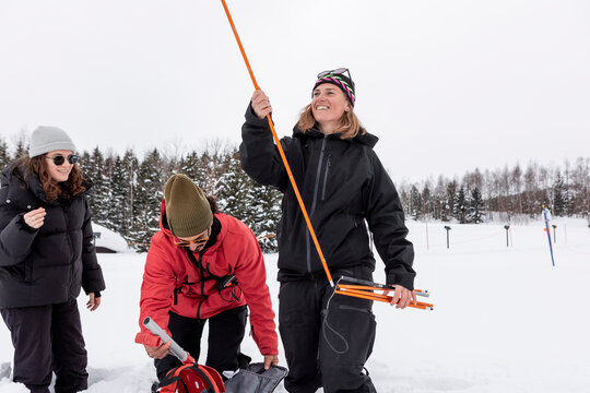Woman holding avalanche probe beside man packing snow gear
