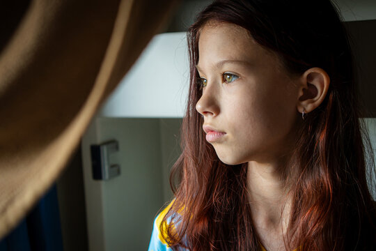 Thoughtful girl looking through window at home indoors