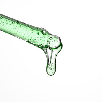 Green cosmetic serum drop from glass pipette on white