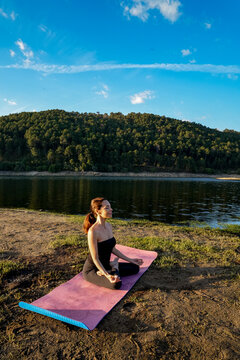 Woman practicing yoga by a tranquil lake at sunset
