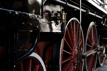 Side view of large, powerful drive wheels on a vintage steam locomotive. The dark metal and red wheels with white accents showcase classic railway machinery and industrial design.  © Grenar