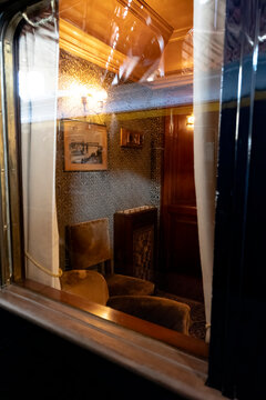 Luxurious vintage train interior with ornate wooden paneling, plush velvet seating, and elegant lighting, viewed through a window. It evokes historical travel and classic railway elegance.
