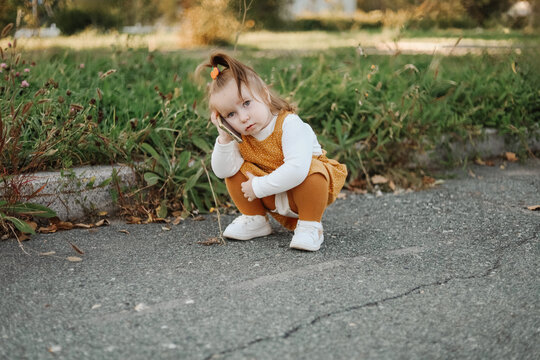 Toddler girl crouching on sidewalk in autumn park