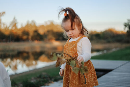 Young girl holding leafy branch by pond near walkway