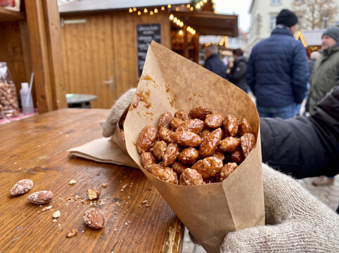 Paper cone of glazed candied almonds held at outdoor Christmas market stall
