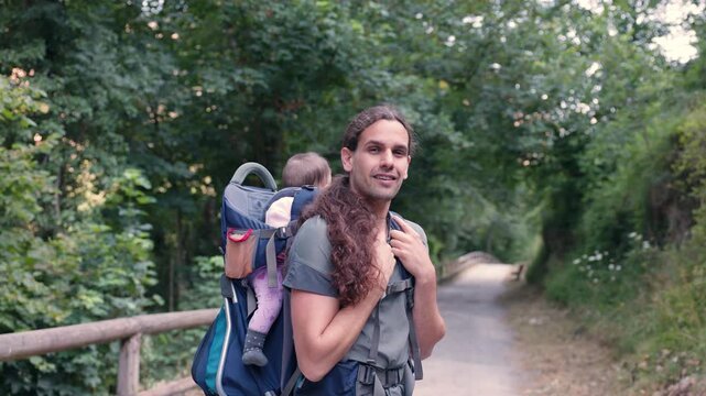 Young father hiking in nature carrying his daughter in a backpack carrier