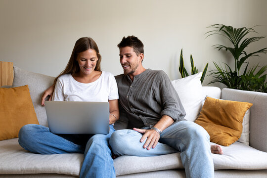 Happy young couple using laptop relaxing sitting on the sofa ordering online.