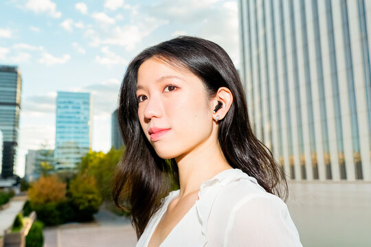 Gen Z Chinese woman wearing earbuds in modern city outdoors