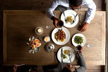 Obraz premium Top view of two people dining with wine and pasta on a wooden table.