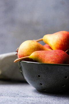 Ripe pears in a black colander on gray background