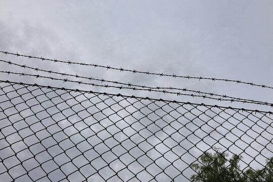 Metal fence with barbed wire. To keep unauthorized out. Cloudy sky.