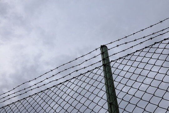 Metal fence with barbed wire. To keep unauthorized out. Cloudy sky.