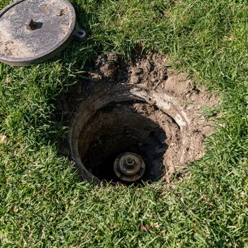 Open water meter pit in residential lawn with lid set aside on grass in morning light