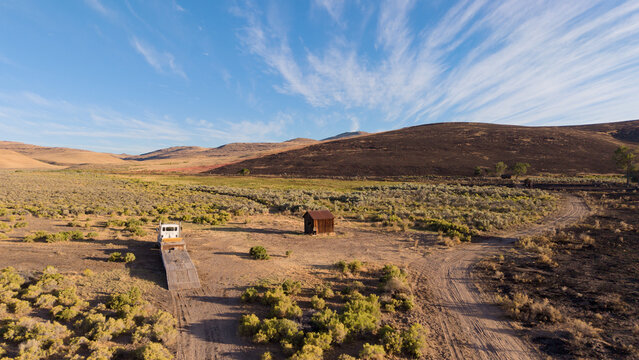 Abandoned line shack and lowbed truck in sagebrush, Lassen County, California; Biscar Fire burn patterns and red retardant staining on hillside.