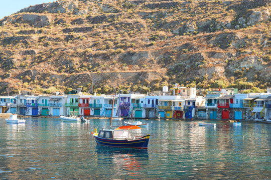 The colorful syrmata boathouses of Klima line the Aegean shoreline on Milos, Greece, creating a vibrant and historic fishing village scene along the bright Mediterranean coast.