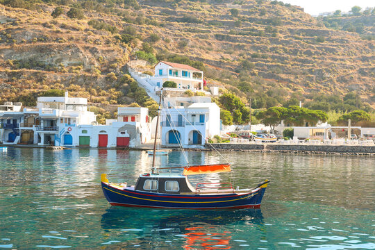 A boat floats in front of colorful syrmata boathouses of Klima line the Aegean shoreline on Milos, Greece, creating a vibrant and historic fishing village scene along the bright Mediterranean coast.