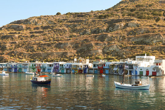 The colorful syrmata boat houses of Klima line the Aegean shoreline on Milos, Greece, creating a vibrant and historic fishing village scene along the bright Mediterranean coast.