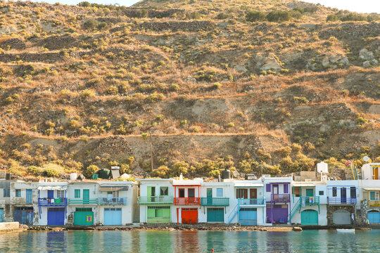 The colorful syrmata boathouses of Klima line the Aegean shoreline on Milos, Greece, creating a vibrant and historic fishing village scene along the bright Mediterranean coast.
