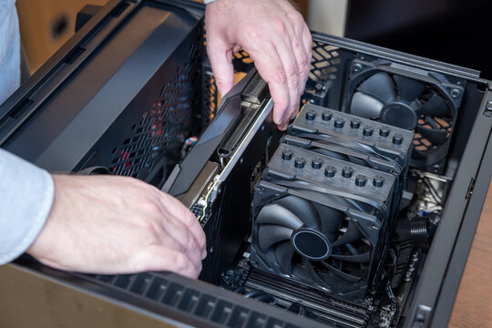 Technician installs a large powerful gaming video card in a gaming PC case. A dual tower CPU cooler is visible nearby. Assembly or upgrade of a powerful gaming PC