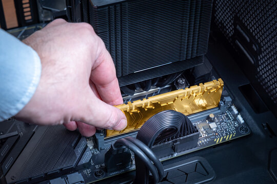 Technician installs gold DDR module into motherboard socket. Concept of rising prices for RAM. Expensive computer components. PC build or upgrade of high-end system