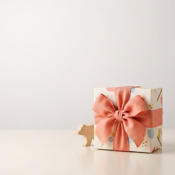 A charming gift box adorned with a coral ribbon bow sits beside a small wooden toy bear, suggesting a thoughtful present for a child's special occasion.