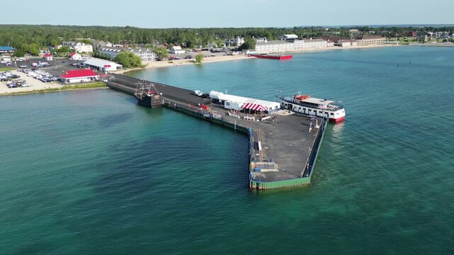 Aerial footage over the historic Mackinac City shoreline. Piers and docks jut from the sandy shoreline for the tour boats to moor. City and bridge alive with adventure and experience