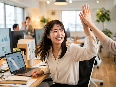 職場で同僚とハイタッチをして喜びを分かち合う明るい笑顔の女性