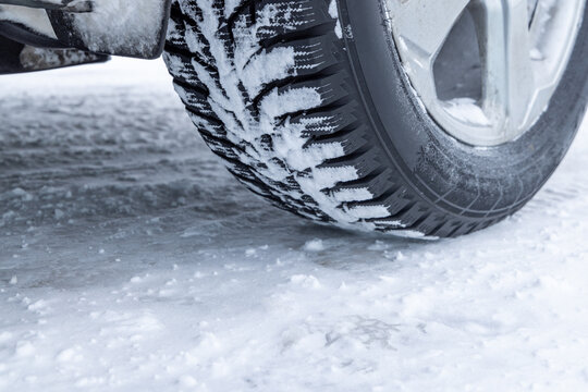 Close-up of a winter vehicle tire resting on a snow-covered icy road, showcasing tread and cold weather conditions.