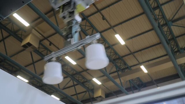 Close up: pick and place robotic arm manipulator with suction cups and lowers white polypropylene yogurt containers: plastic injection molding machine at exhibition, factory, trade show