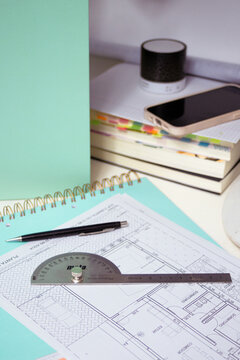 Desk setup showing architectural blueprints with a protractor, pen, and notebook, symbolizing engineering, design, and diligent project planning in a professional workspace