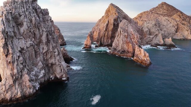 Dramatic aerial flight over granite cliffs and sea pass at The Arch in Cabo San Lucas at dawn