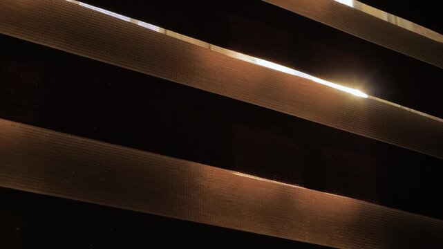 Sun light is shining through the window blinds - view from dark room: sun lens flare, close up, selective focus. Morning, indoors, b-roll and abstract concept