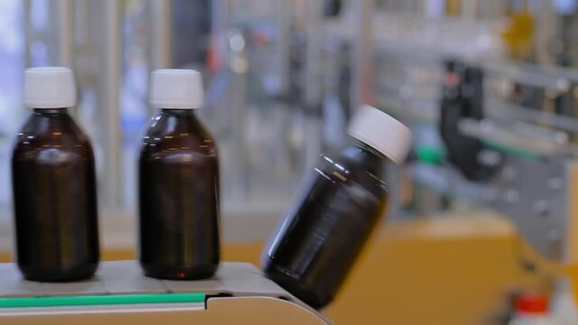 Side view, close up: production line, conveyor belt of bottle shrink sleeve labeling machine with empty amber glass bottles at plastic packaging exhibition, trade show or factory: demonstration mode