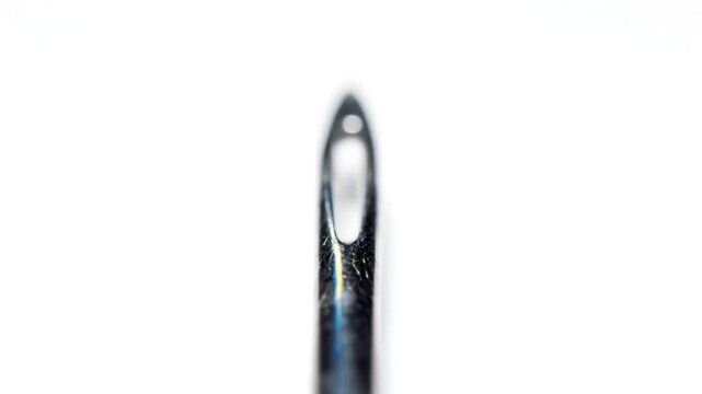Extreme close-up view of a sewing needle's eye against a bright white background, macro detail