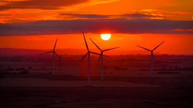 Wind turbines silhouetted against a fiery sunset over rural Sussex, England; ideal for renewable energy, sustainability, climate, technology and business advertising