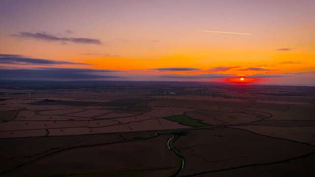 Wind turbines silhouetted against a fiery sunset over rural Sussex, England; ideal for renewable energy, sustainability, climate, technology and business advertising