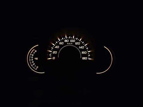 Illuminated car instrument cluster at night featuring a speedometer and tachometer, highlighting modern dashboard design with glowing gauges in a dark vehicle interior