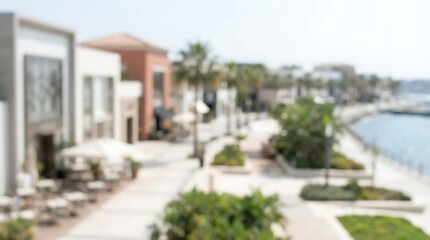 Fototapeta premium A blurred view of a waterfront promenade with modern buildings, palm trees, and outdoor cafes by the sea.
