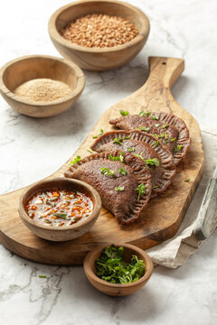 Buckwheat flour empanadas served with sauce and cilantro on a wooden board in a kitchen setting