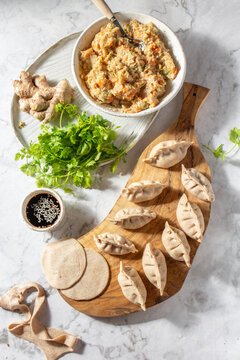 Making dumplings with filling, fresh ingredients, and dough on a wooden board in a kitchen space