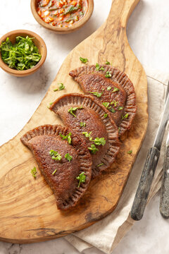 Buckwheat flour empanadas served with sauce and cilantro on a wooden board in a kitchen setting