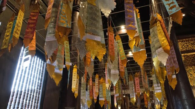 Colorful traditional Thai Tung prayer flags hanging from the ceiling inside the Thai temple hall creating a festive sacred atmosphere