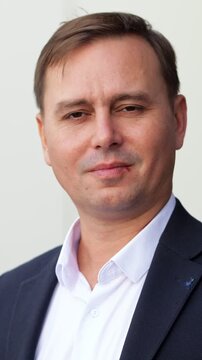 Handsome middle aged businessman in a suit smiling at the camera and showing a thumbs up gesture, expressing success and approval against a clean white background in a corporate setting