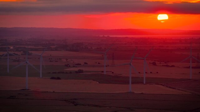 Wind turbines silhouetted against a fiery sunset over rural Sussex, England; ideal for renewable energy, sustainability, climate, technology and business advertising
